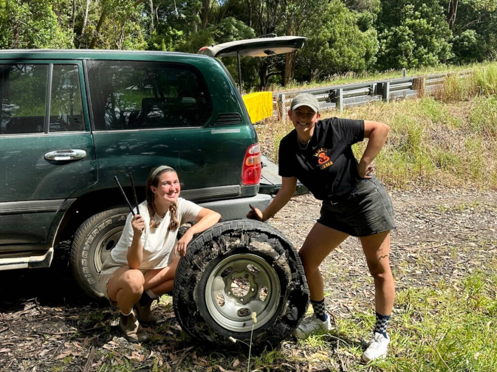 Author Laura and her friend posing for a photo with the shredded tire on the side of the road