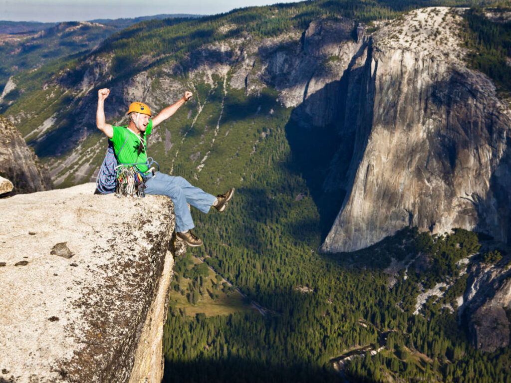 A rock climber celebrating on the summit while sitting on the cliff