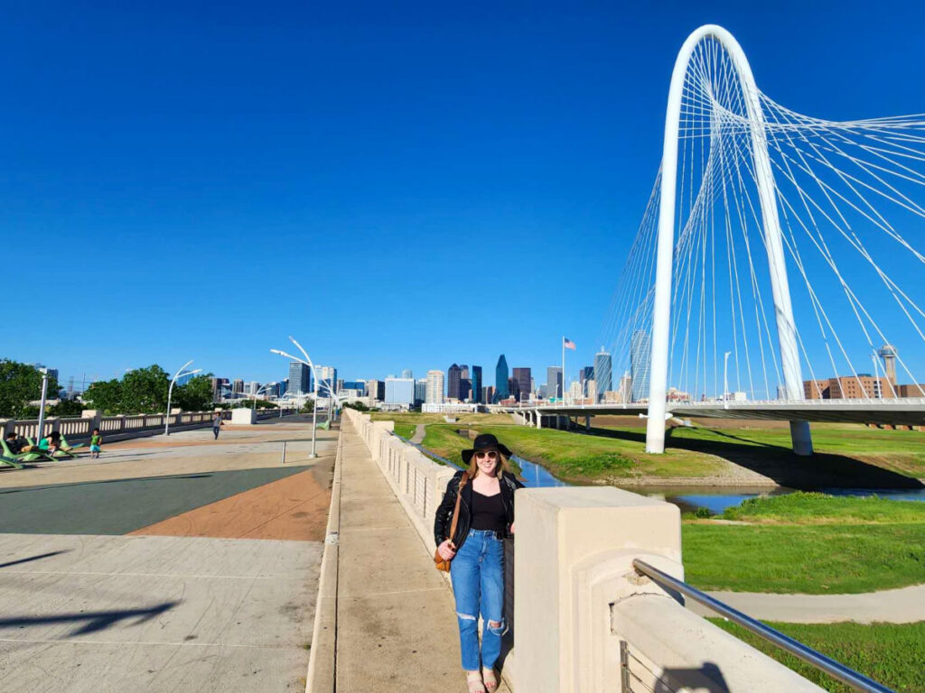 Author Sarah Heath poses on Ronald Kirk Pedestrian Bridge with city skyline backdrop near Trinity Groves