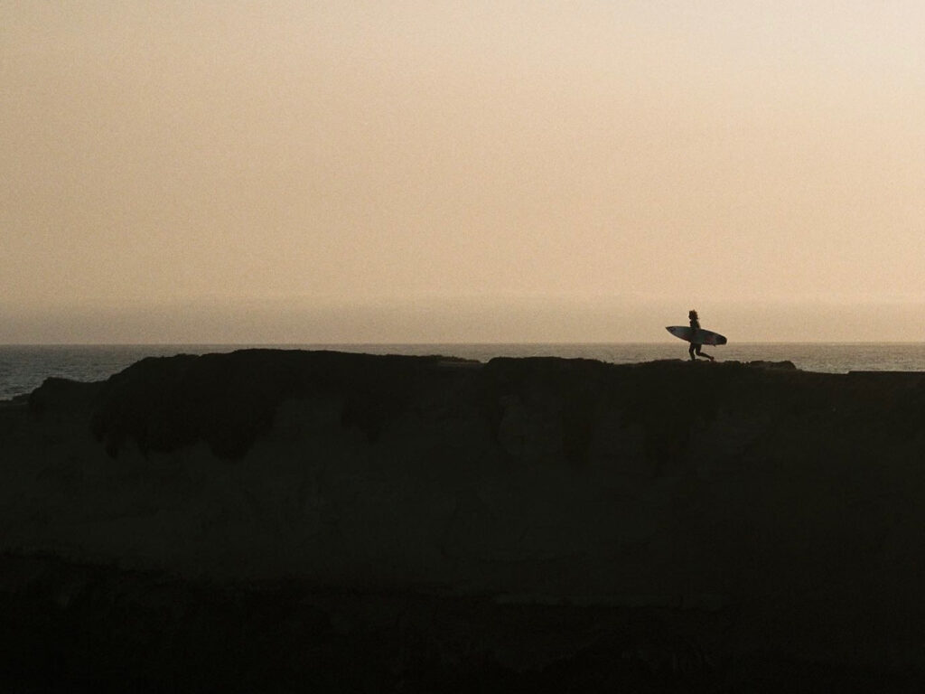 A surfer holding a surfboard while running at Steamer Lane at sunset