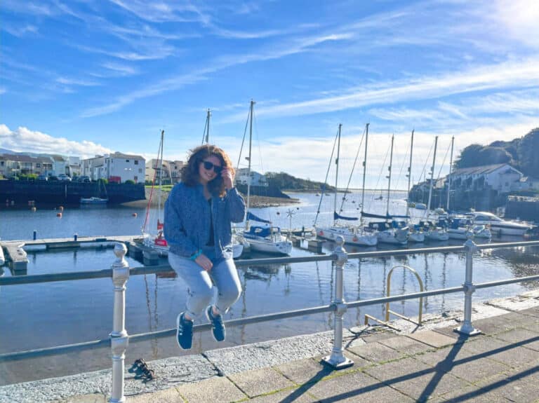 The author Ruthie Walters, posing for a photo while sitting on the railing at Porthmadog Harbour