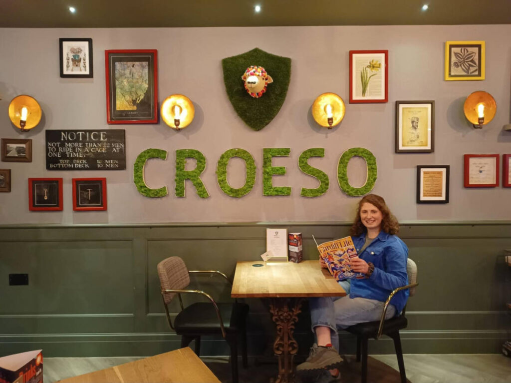 The author Ruthie Walters, sitting near the huge signage of Croeso