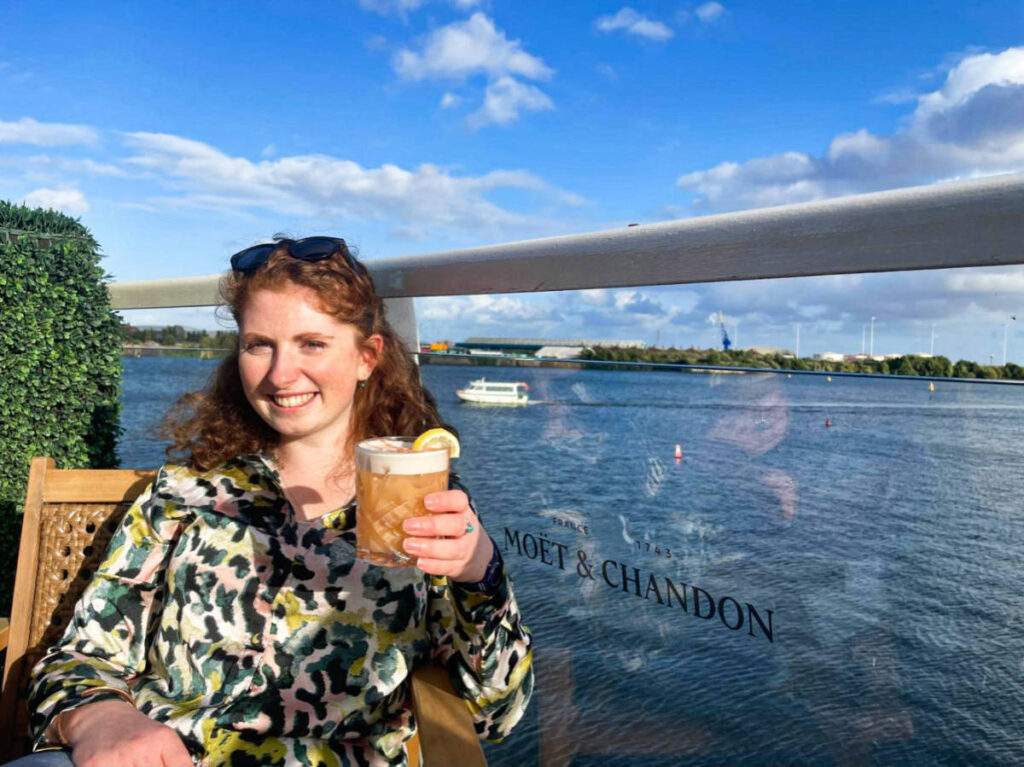 The author Ruthie Walters, holding a glass of cocktail at Tir a Môr