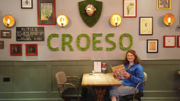 The author Ruthie, sitting near the Croeso signage in Hotel Indigo
