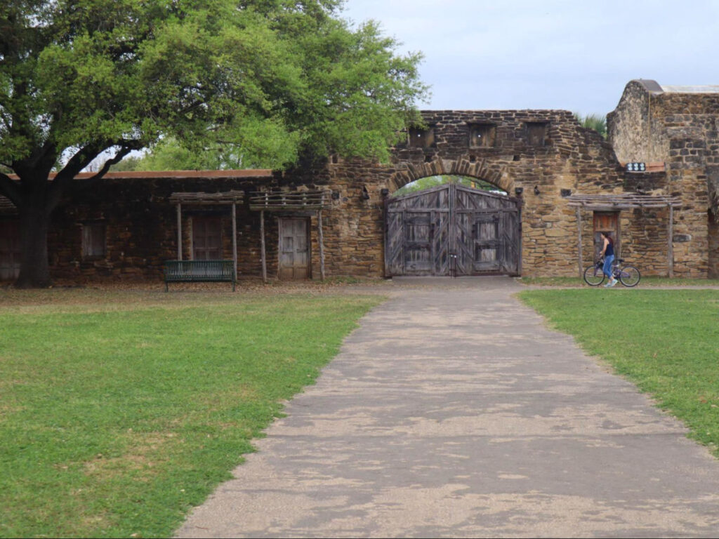 A lady biking in front of a gate in San Antonio Missions National Historical Park