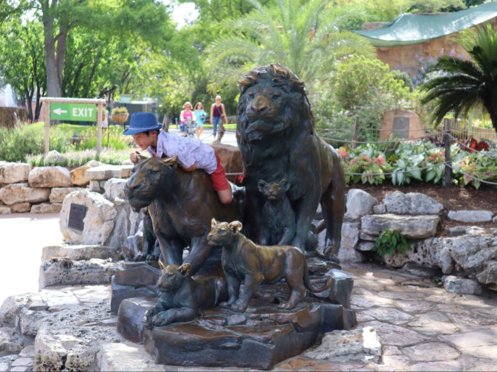 A kid riding the lion statue at the entrance of San Antonio Zoo