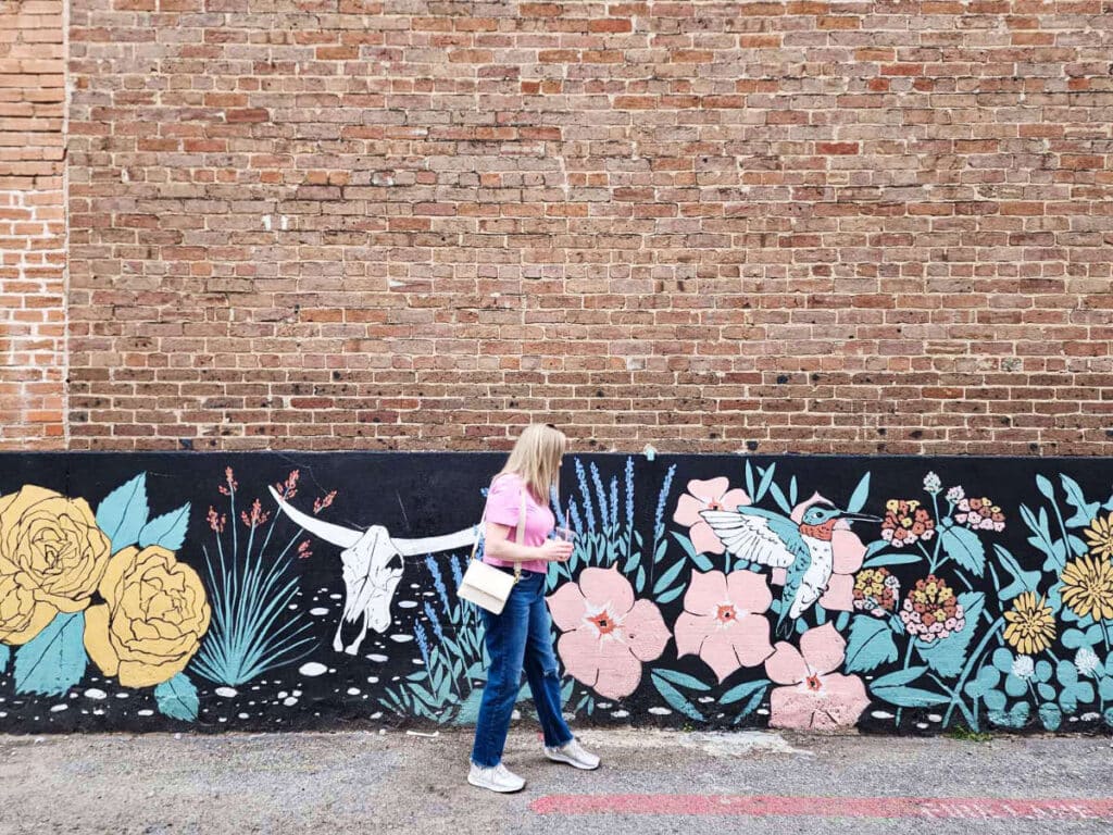 The author Sarah Heath, walking against the Mckinney’s historic buildings with eclectic mural art
