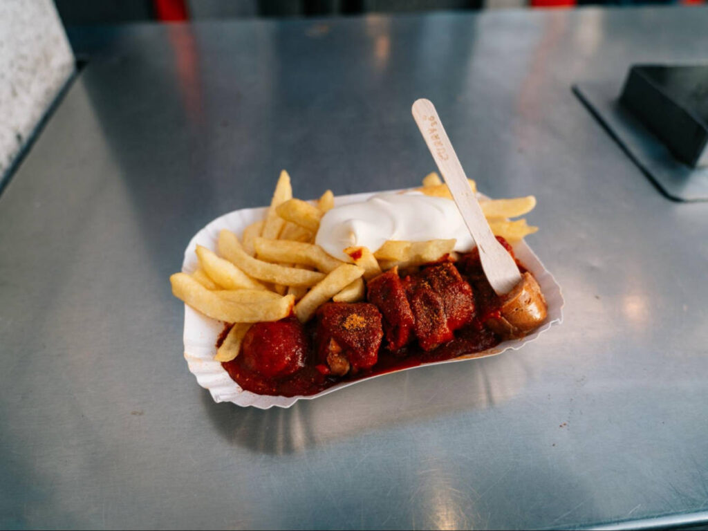 Closeup look of the smoked sausage drenched in curry-flavored sauce with fries