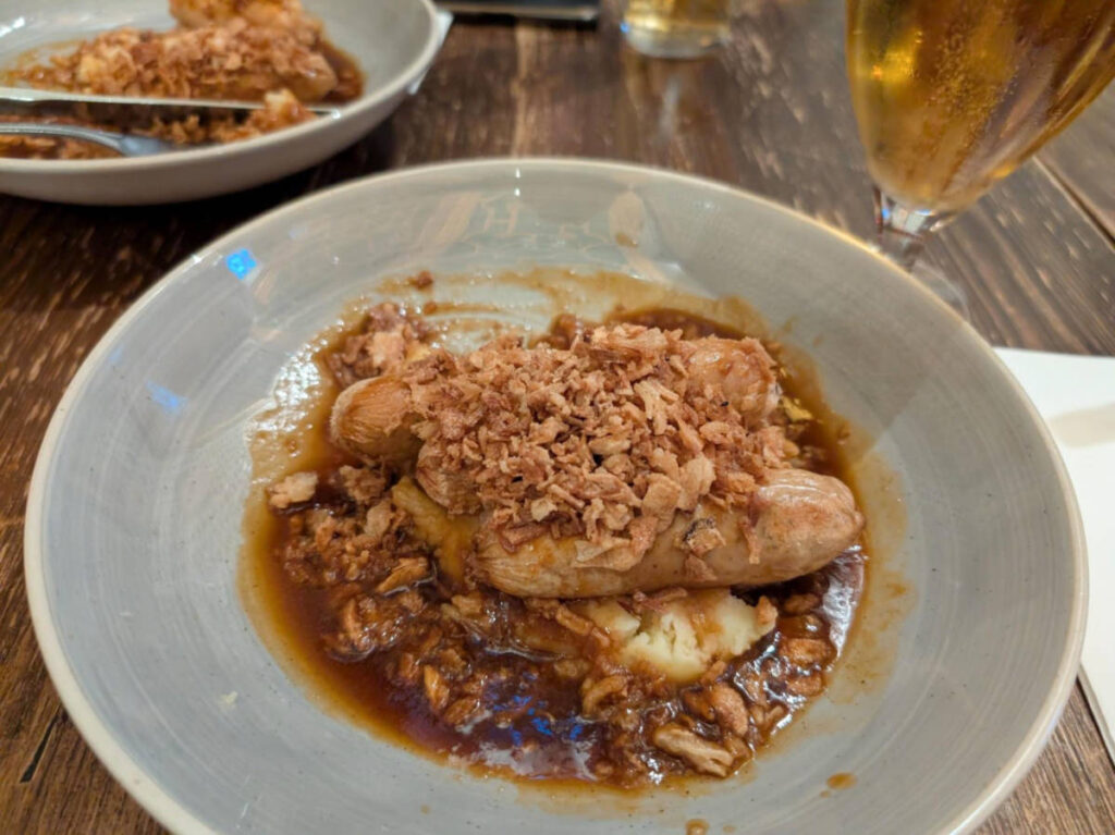 Closeup look of the bangers, mash and crispy onion in a rich gravy served on the plate