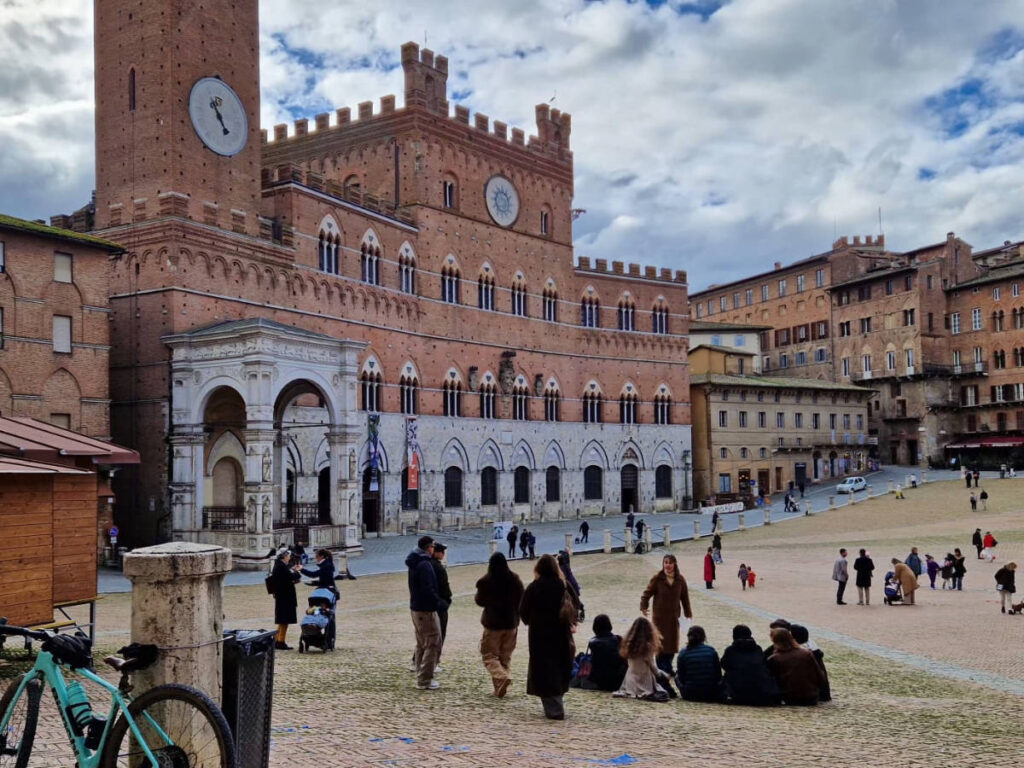 People sitting on the lawn in front of the Piazza del Campo
