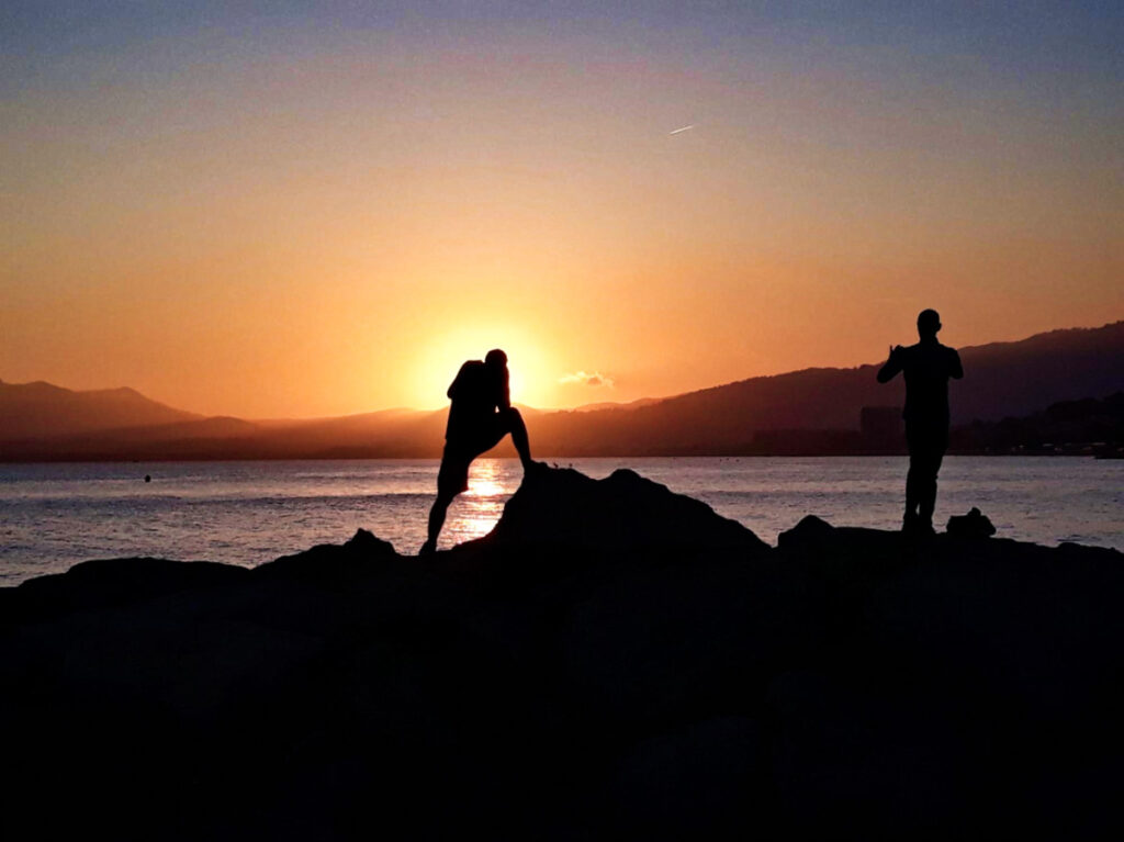 View of the silhouette of the men on top of the cliff overlooking the ocean at sunset