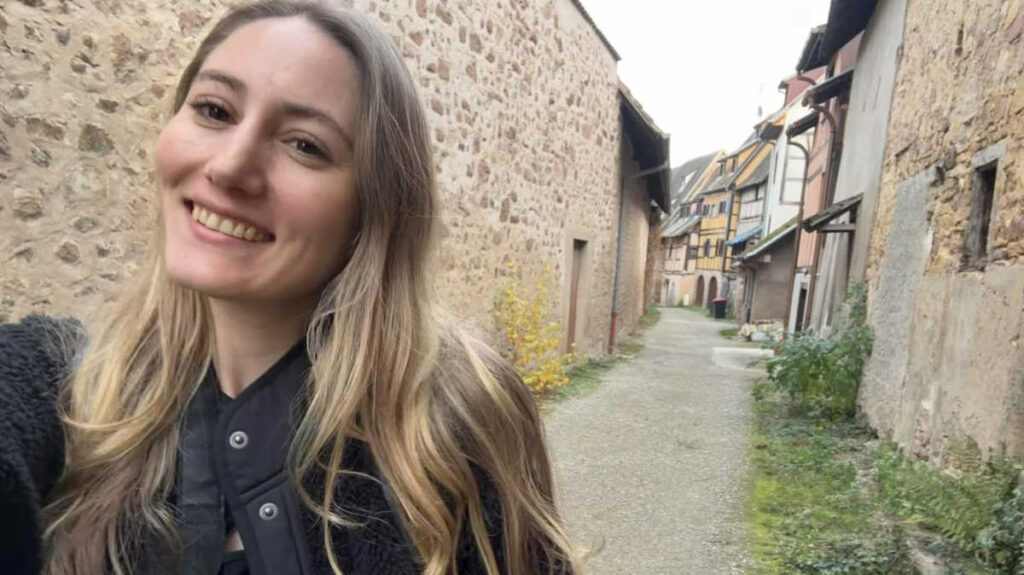 The author Sky Ariella, smiling for a photo on a cobbled street in the Alsace region