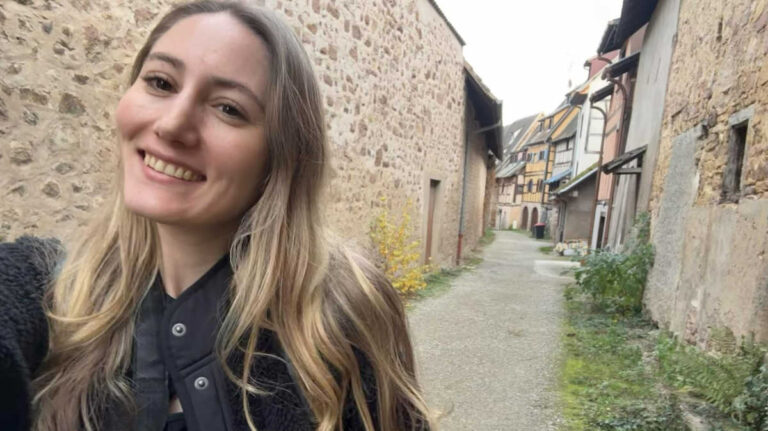 The author Sky Ariella, smiling for a photo on a cobbled street in the Alsace region