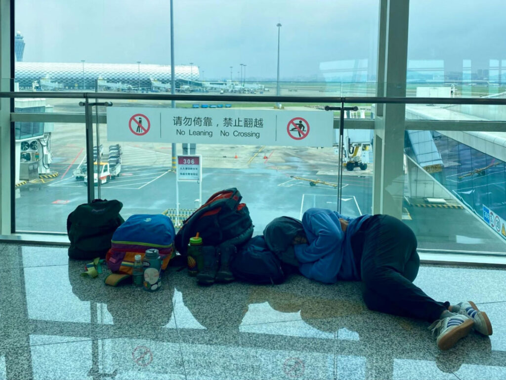 A person sleeping on the floor of the airport with all their bags