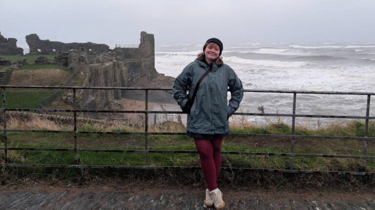 The author, Louise Wylie smiling for a photo with the ruins of St Andrews on her background