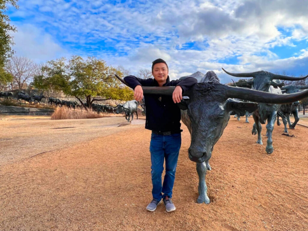 Man posing with bull statue at Pioneer Plaza
