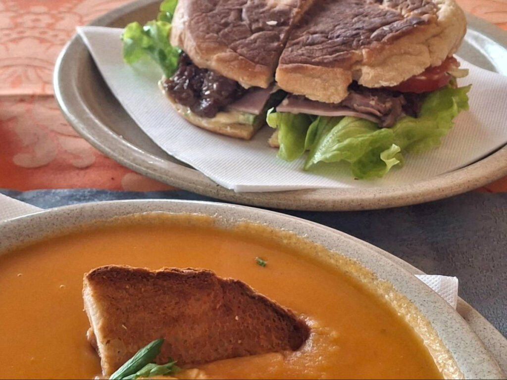 A steak sandwich on a Bolo do Caco with tomato soup on the side