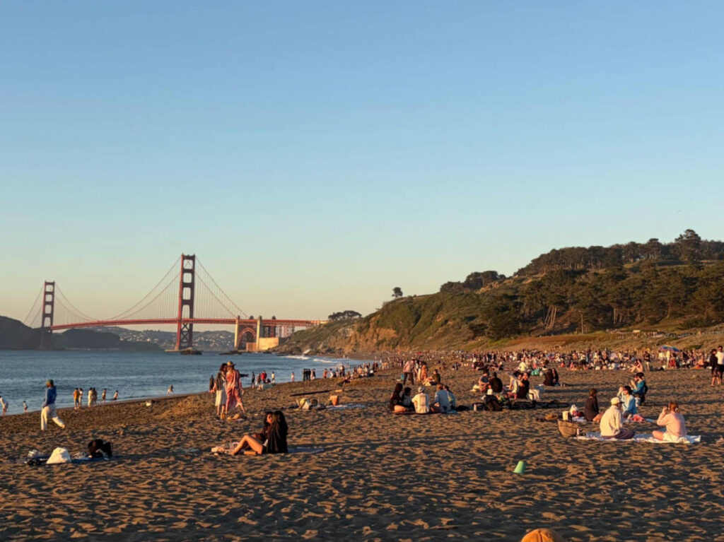 People chilling at the Baker Beach with the view of the Golden Gate Bridge at sunset