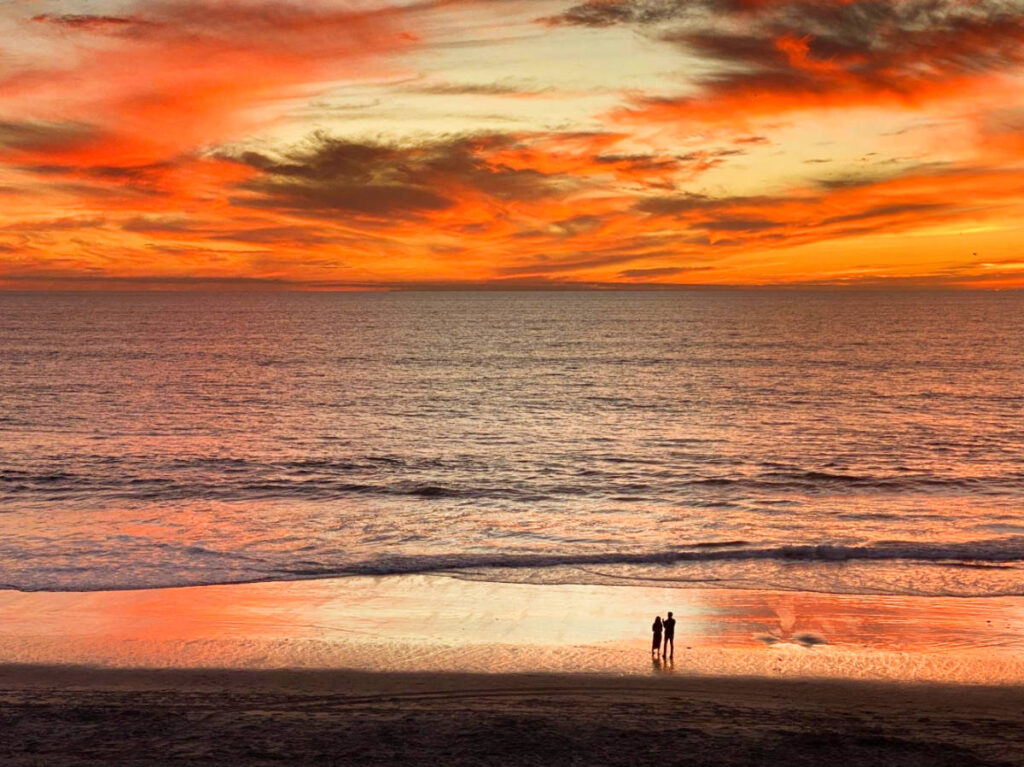 A couple watching the scenic view of the sunset over the beach