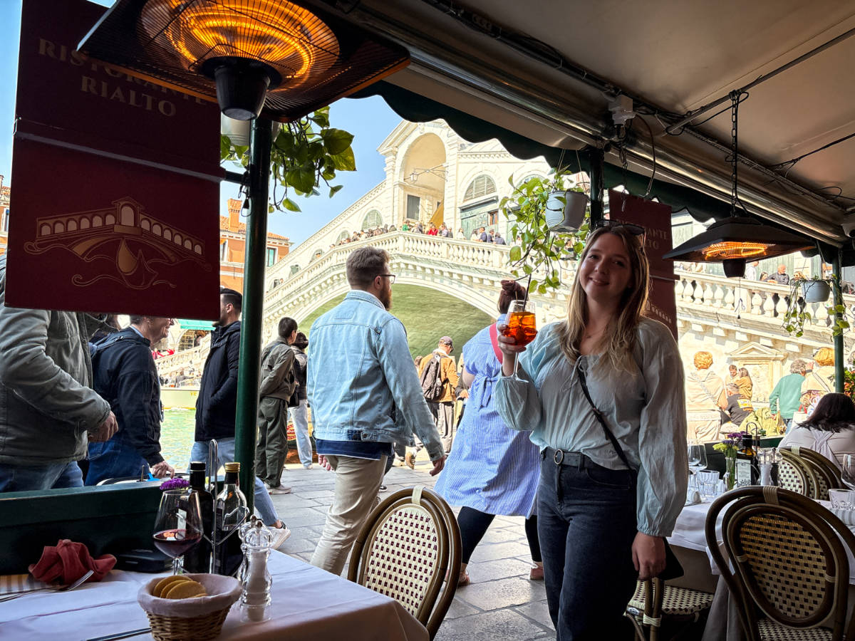 The author Taylor Herperger, holding her drink at the Rialto Hotel with the view of the Rialto Bridge