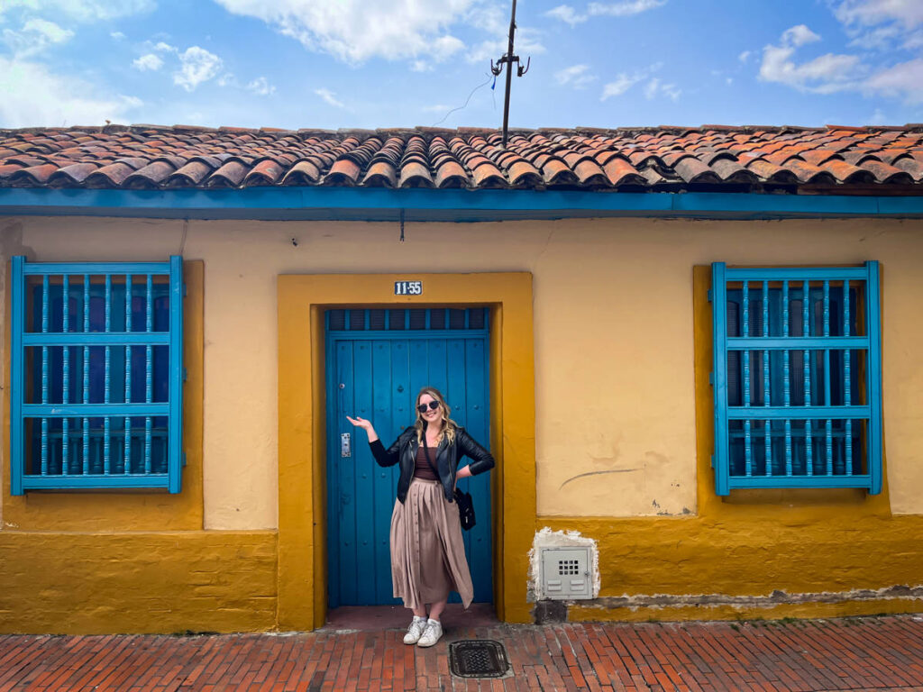 The author Taylor Herperger, posing for a photo in fornmt of the vibrant blue and yellow building in Bogota