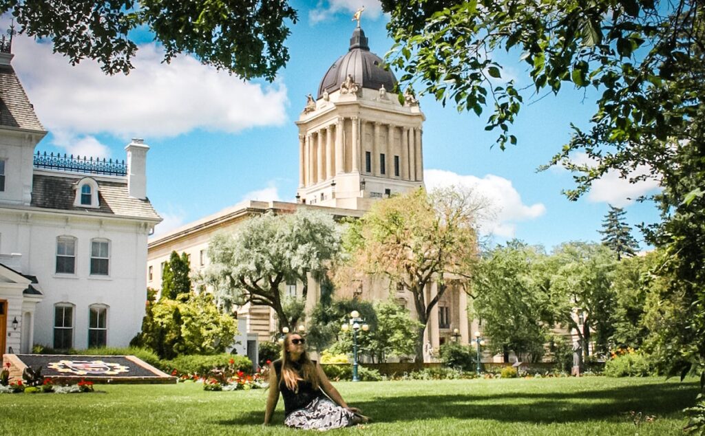 Author Taylor sits in front of the Legislative building in Winnipeg Canada on a summer day