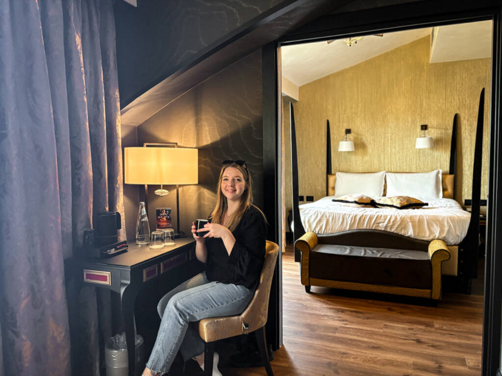 The author Taylor Herperger, sitting while holding a drinking in her suite at Palazzo Veneziano