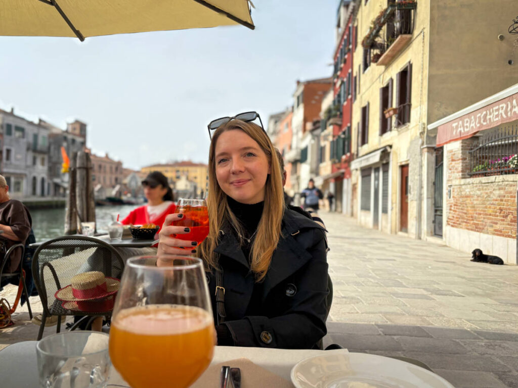 The author Taylor Herperger, holding a glass of Aperol Spritz by the Cannaregio Canal