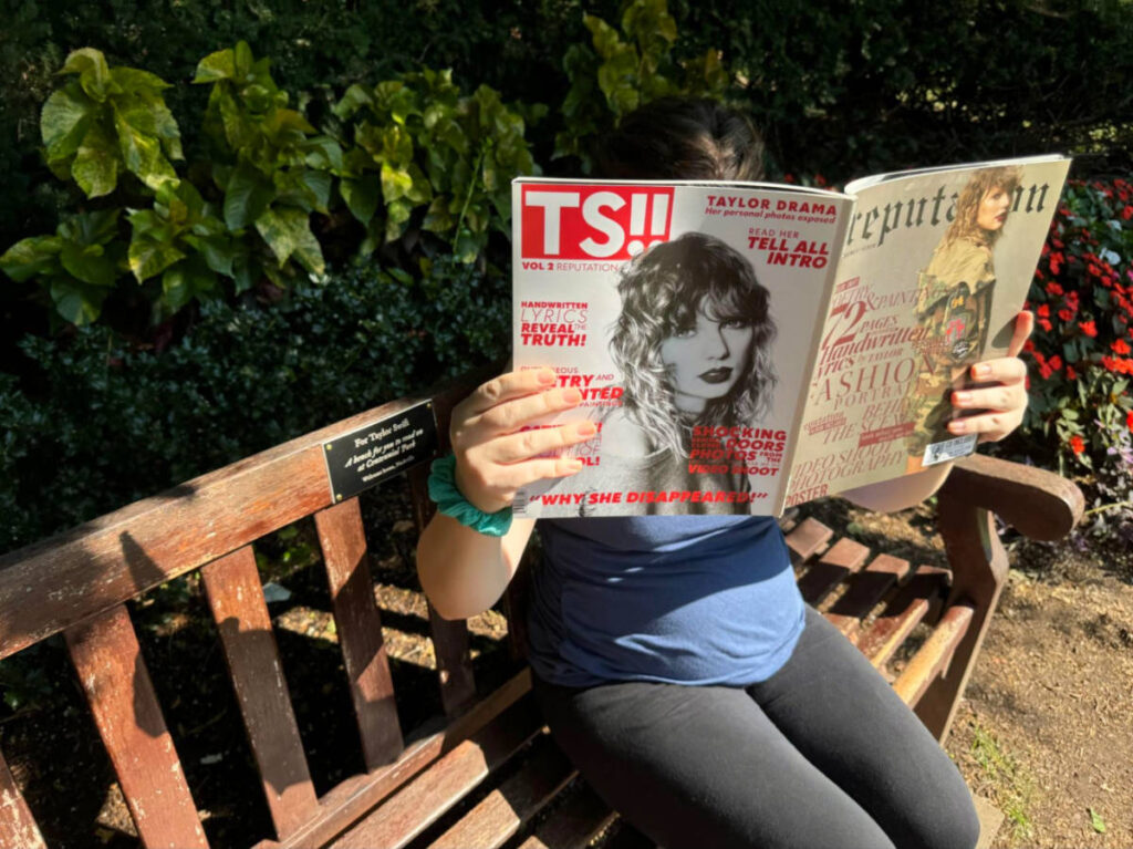 Author Elizabeth sitting on the Taylor Swift Bench while reading a TS magazine