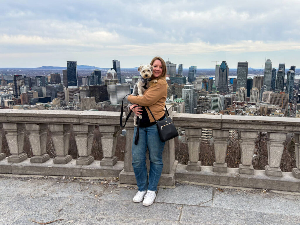 The author Taylor Herperger holding her puppy Gustavo at a balcony with an overlooking view of Montreal skyline