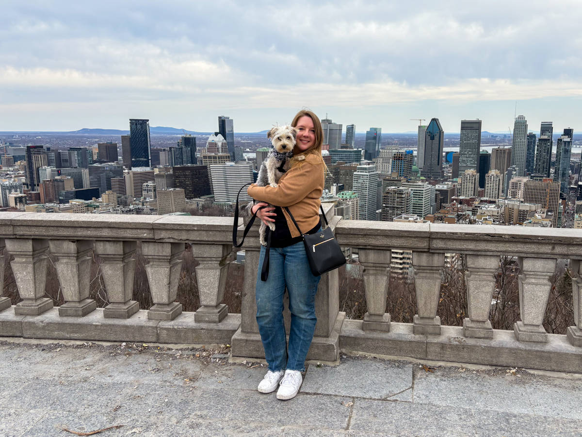 The author Taylor Herperger holding her puppy Gustavo at a balcony with an overlooking view of Montreal skyline