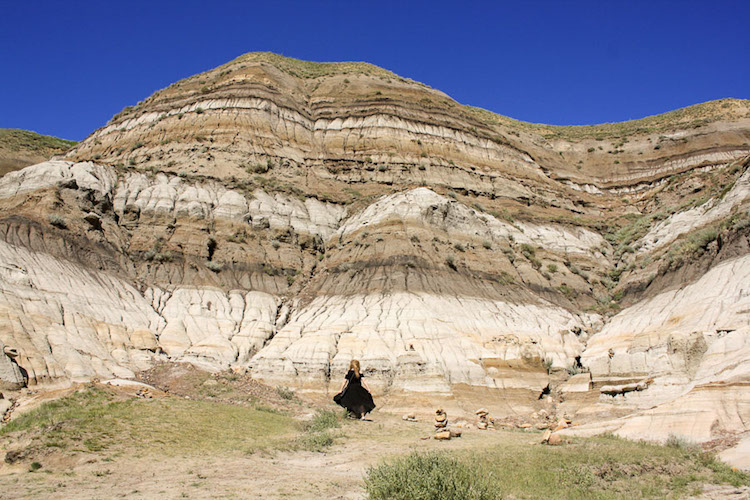 The author Taylor Herpeger at the bottom of multi-layered rock against a blue sky in Drumheller