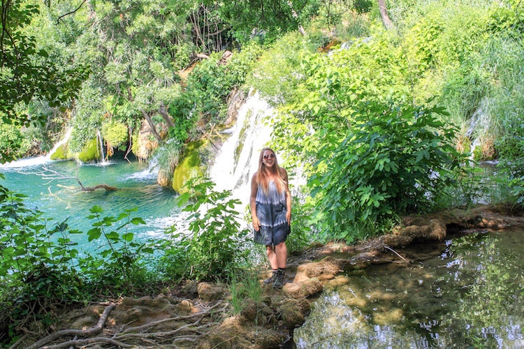 Taylor stands in front of a turquoise lake and waterfall at Krka National Park