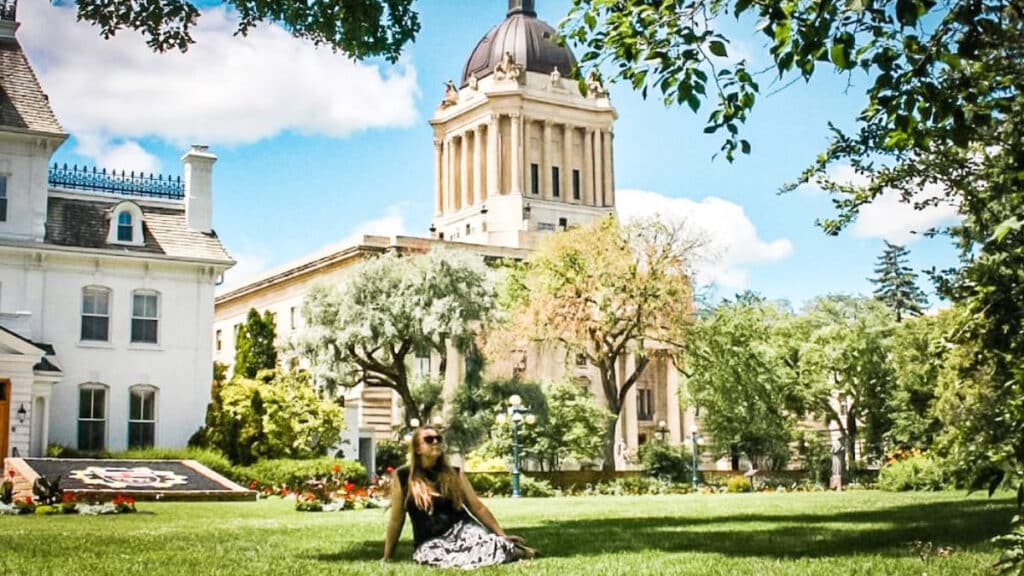 The author Taylor Herperger, sitting on the lawn in front of the Manitoba Legislature in Winnipeg