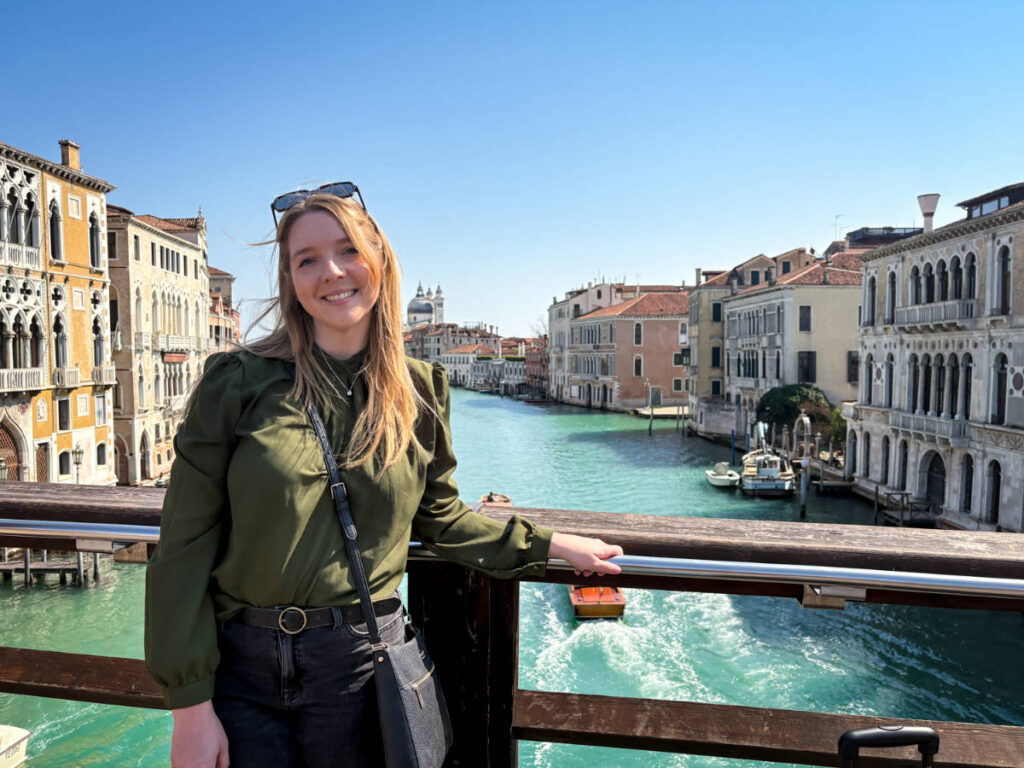 The author Taylor Herperger, smiling for a photo with an overlooking view of the canal at the Ponte dell’Accademia