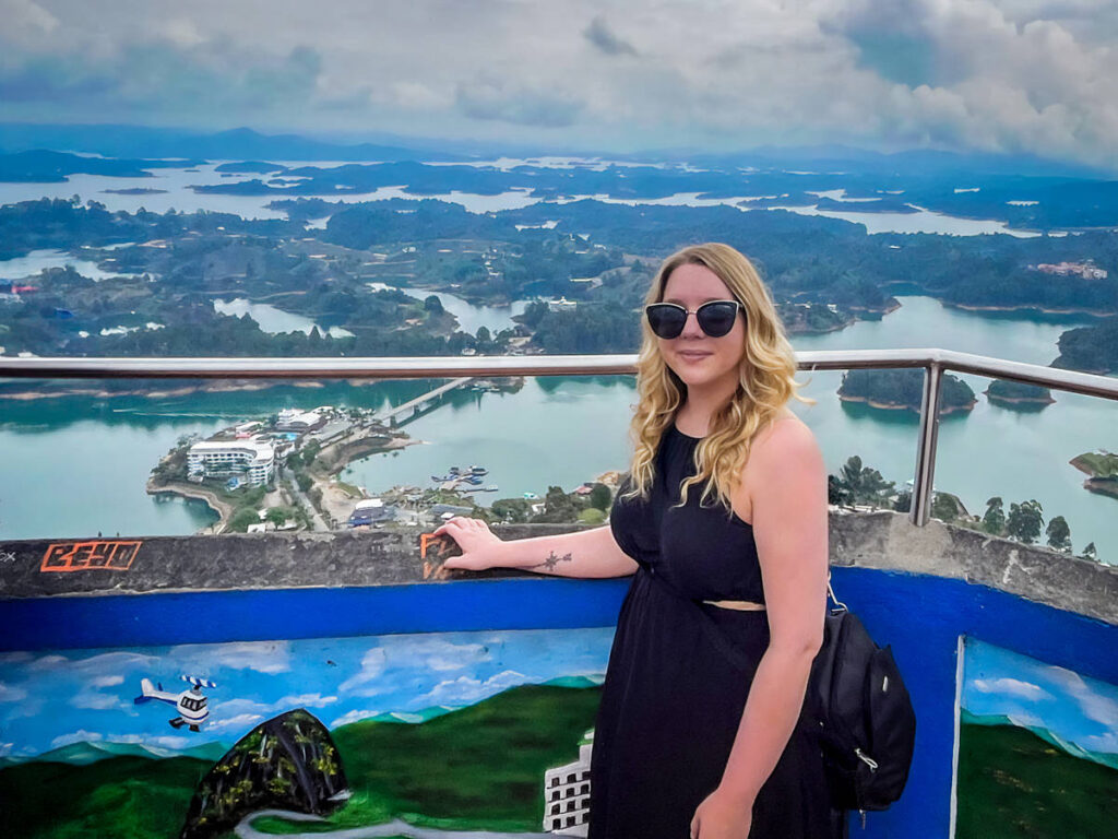 The author Taylor Herperger, smiling for a photo with an overlooking view of Antioquia at the top of la Piedra del Peñol