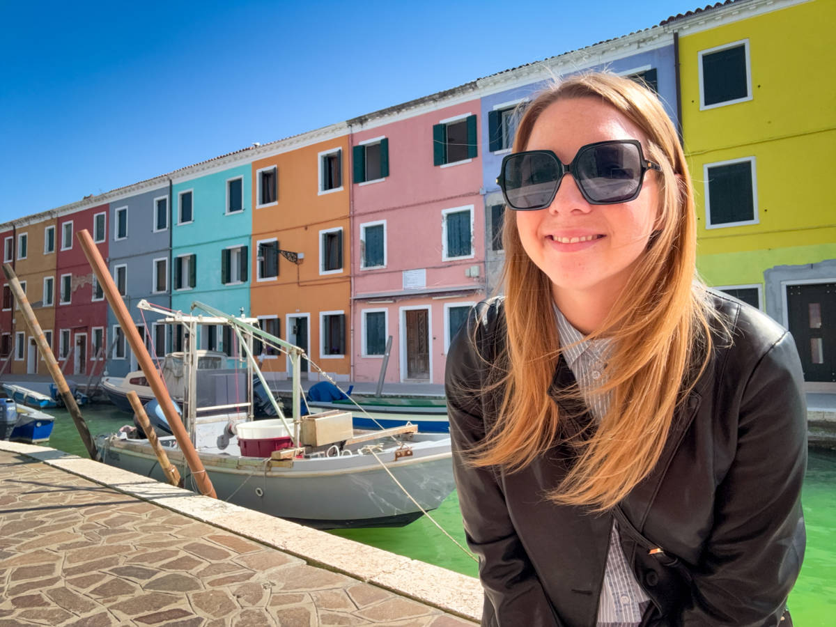 The author Taylor Herperger, smiling for a photo in front of the colorful buildings in Burano