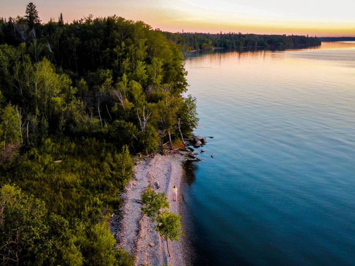 Aerial view of the author Taylor Herperger, walking along the shoreline surrounded by greenery in Hecla Provincial Park