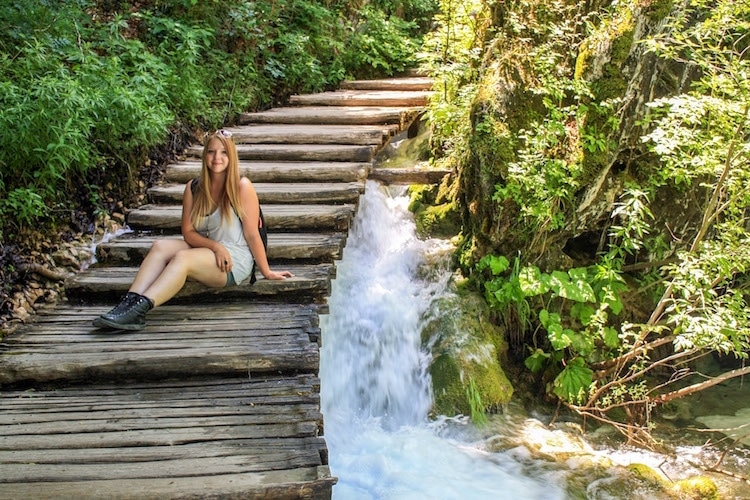 Taylor sits on wooden steps over a waterfall in Plitvice Lakes National Park