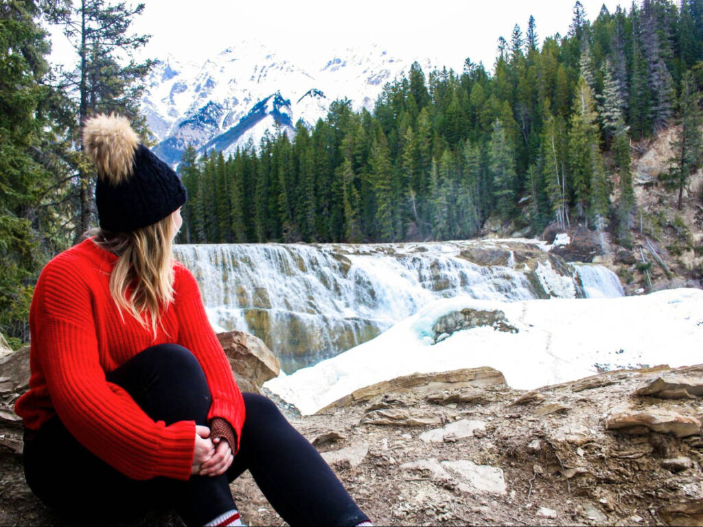 The author Taylor Herperger, sitting on the rocky surface while overlooking the falls in Yoho National Park