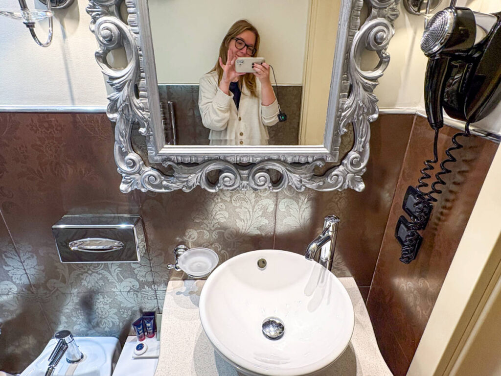 The author Taylor Herperger, smiling for a photo in front of the bathroom mirror