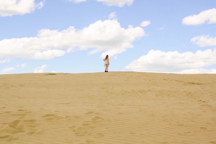 Taylor stands on top of a sand dune beneath blue skies in the Great Sandhills of Saskatchewan