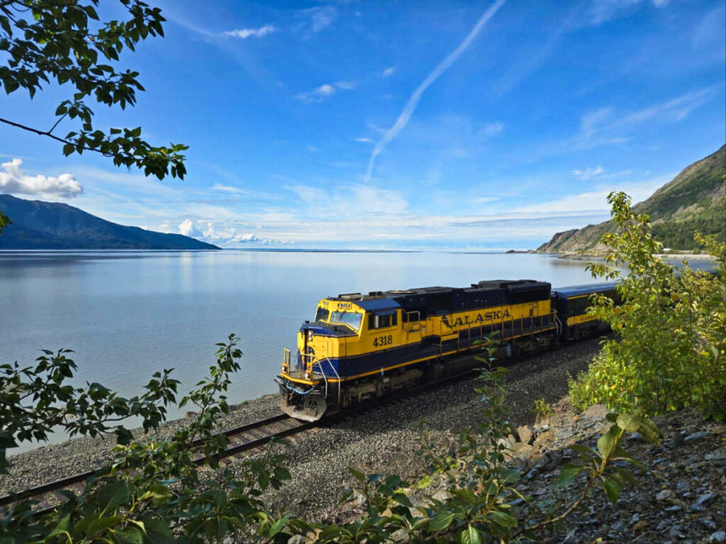 A vibrant yellow Alaska Railroad passing the scenic views of Cook Inlet