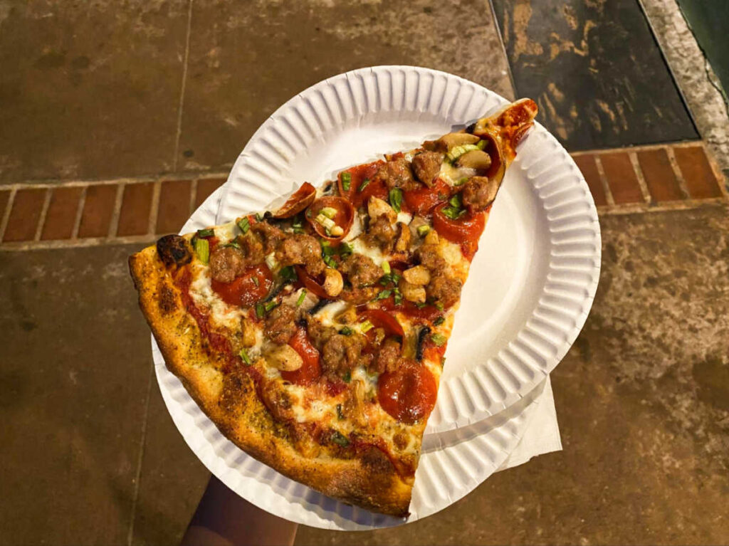 A sliced Big Sur pizza on a paper plate