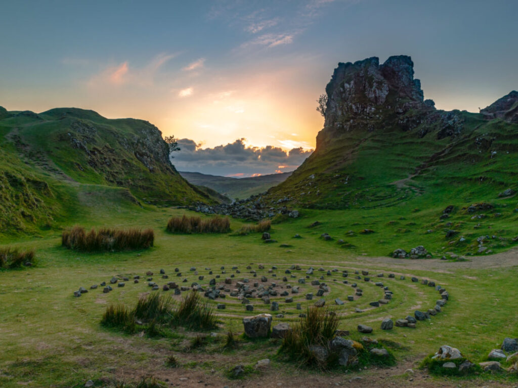 View of sun setting over circular stone circle in grassy field at The Fairy Glen, Skye