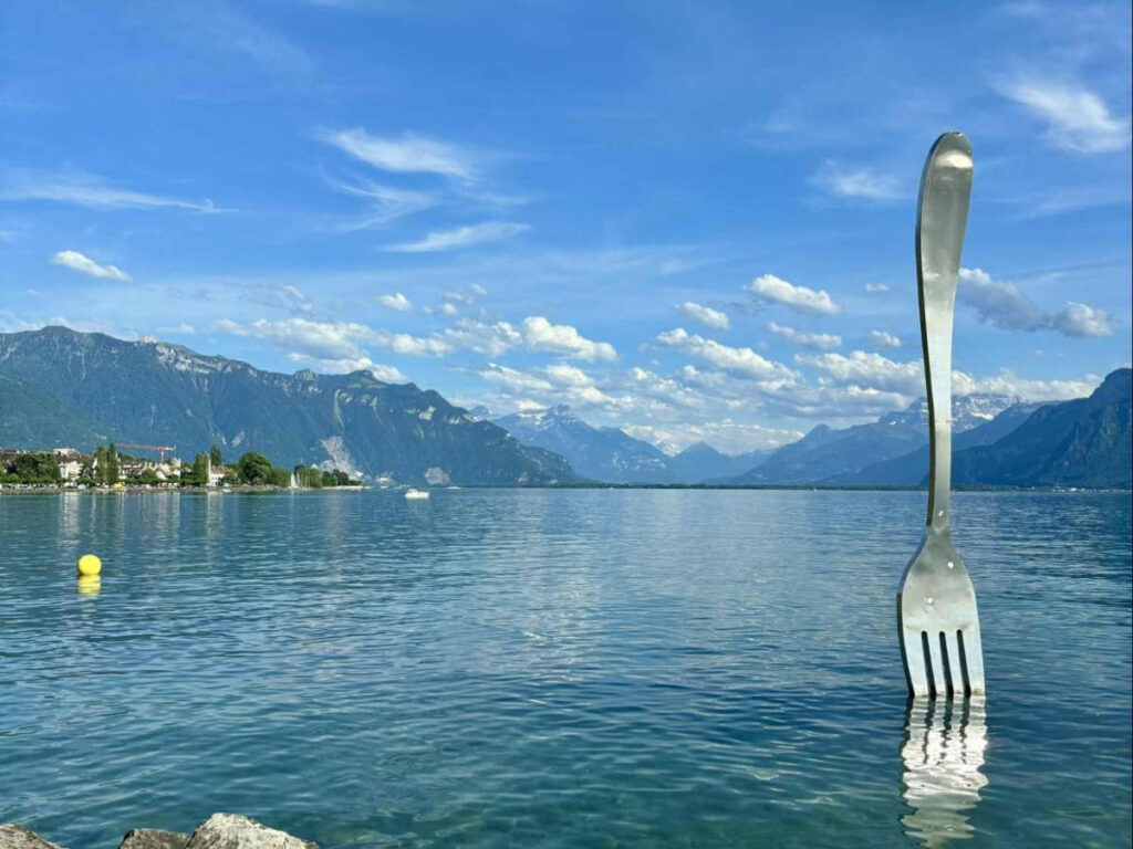 A giant fork sculpture on the lake with scenic mountain views in the background