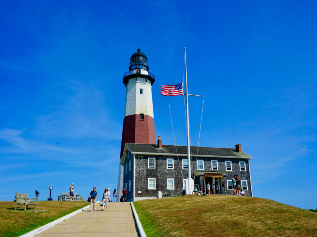 Montauk Lighthouse, with the USA flag waving in front of it on a sunny day