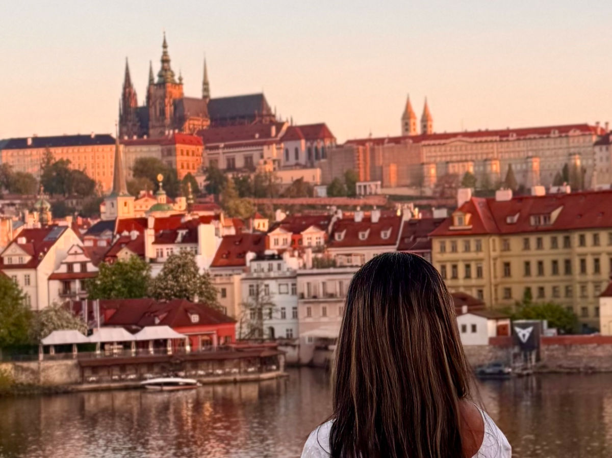 Author Meera looking at the view of the Prague Castle from the Charles Bridge at sunrise
