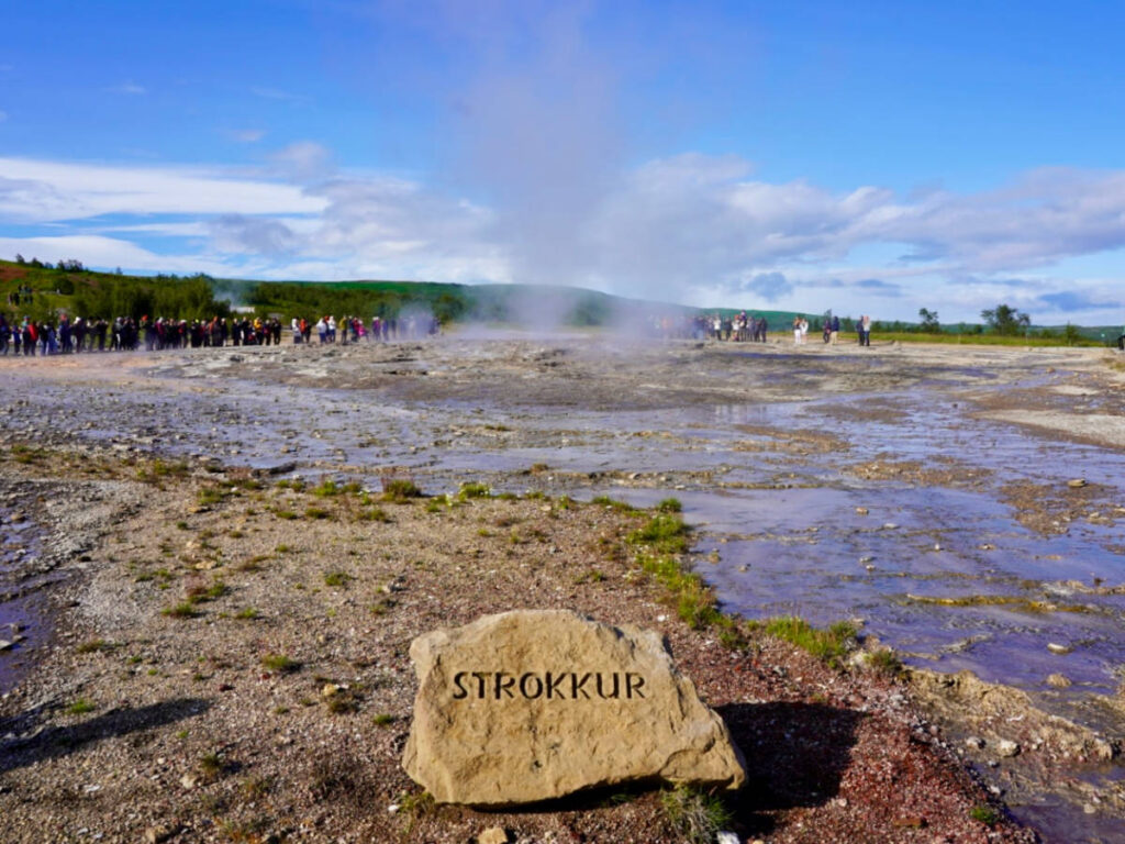 A stone with the Strokkur text engraved into it and a crowd of people in the background
