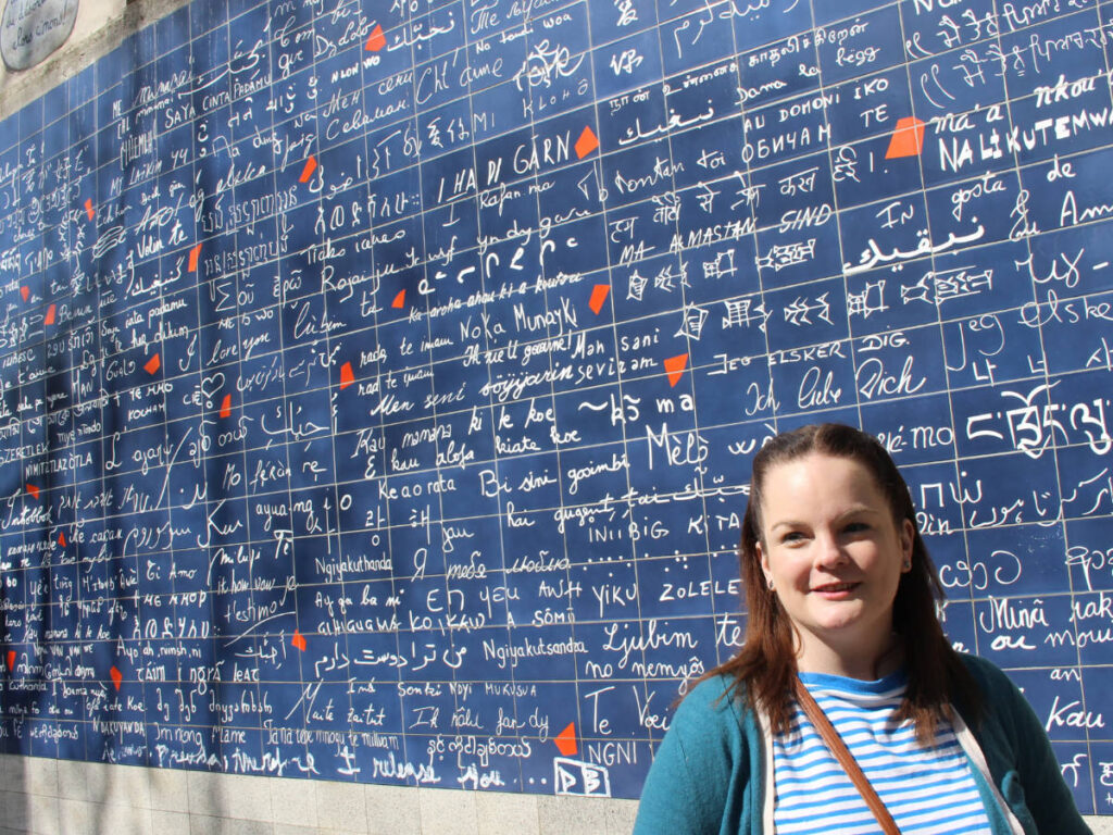 The author, Rachel Kapelke Dale posing for a photo in front of the “Mur des je t’aime”